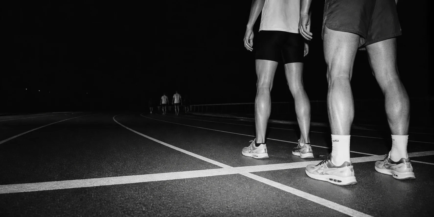 Two runners waiting behind a track starting line at night